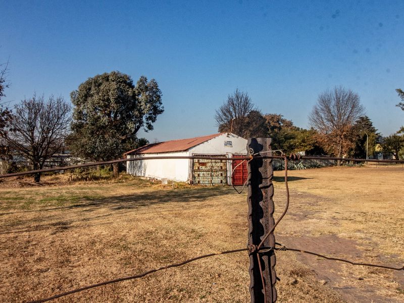 View of a commercial outbuilding with a corrugated metal roof, set within a large open yard enclosed by wire fencing.
