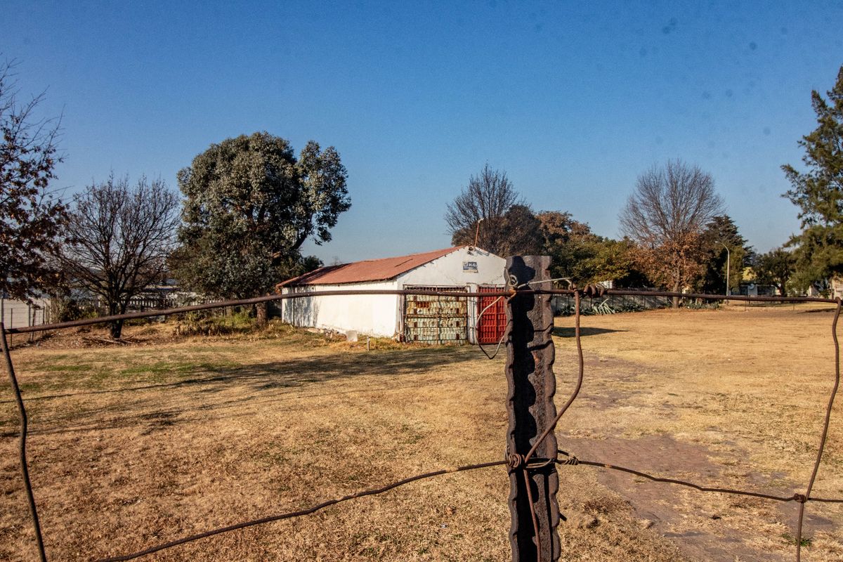 View of a commercial outbuilding with a corrugated metal roof, set within a large open yard enclosed by wire fencing.