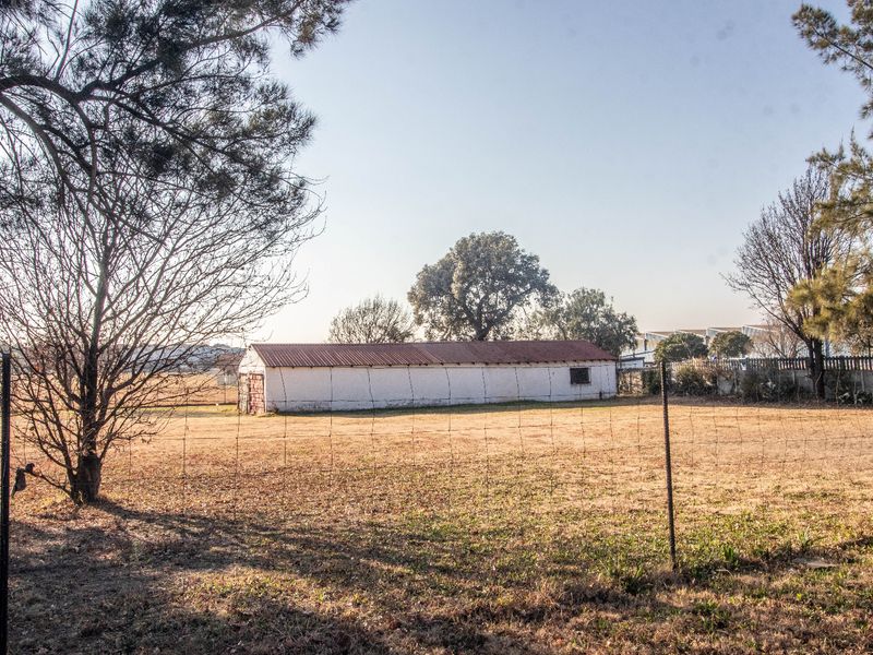 A view of a detached commercial outbuilding or storage structure situated on a large, open plot of land with perimeter wire fencing.