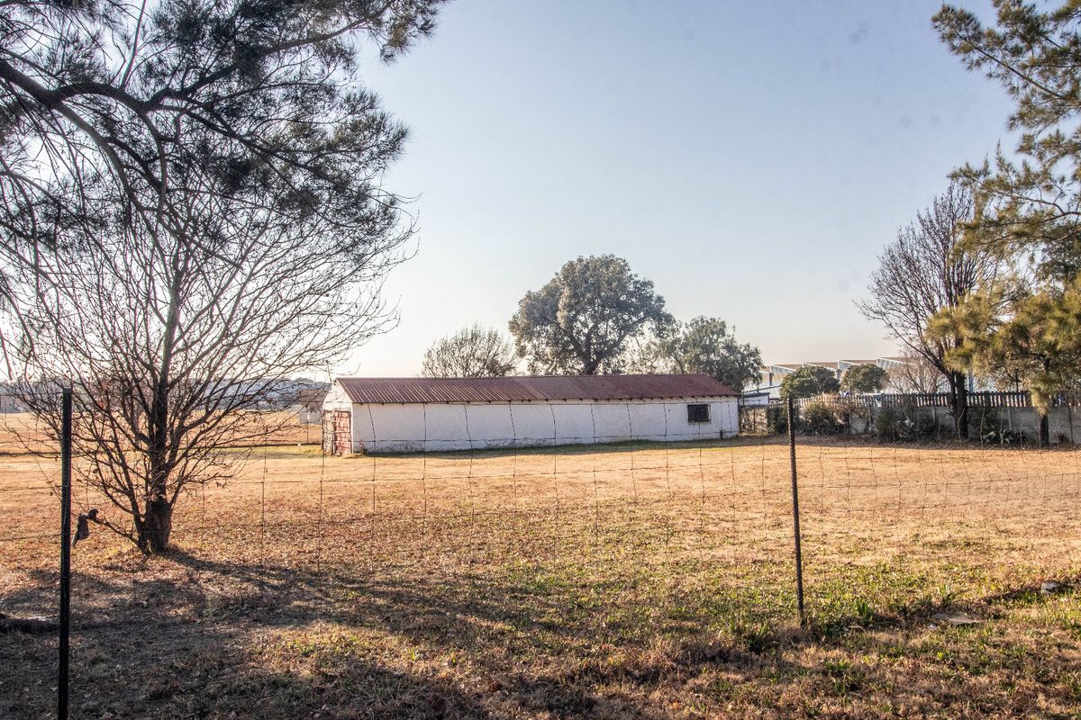 A view of a detached commercial outbuilding or storage structure situated on a large, open plot of land with perimeter wire fencing.