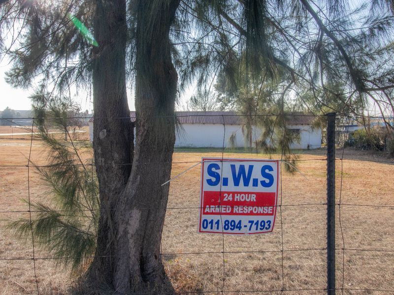 View of a large open plot with a wire fence, mature tree, and a distant outbuilding structure.
