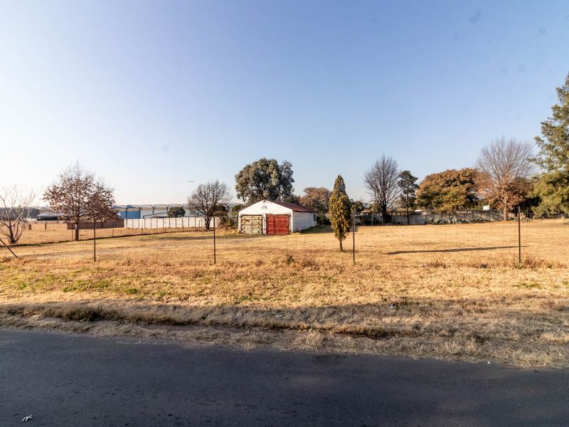 A wide view of a large, undeveloped commercial plot featuring a detached garage structure and perimeter wire fencing.