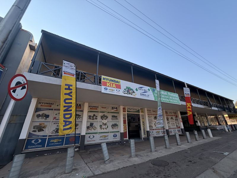 Front elevation of a commercial building featuring a ground-level storefront with signage and an upper-level covered balcony with metal railings.