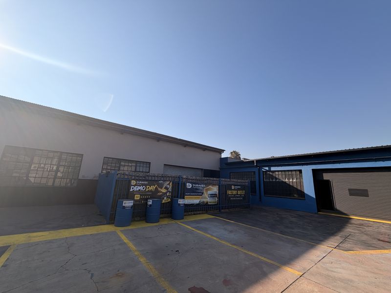 Commercial property exterior featuring a paved yard area, roller shutter access, and secure perimeter fencing, suitable for industrial or retail operations.