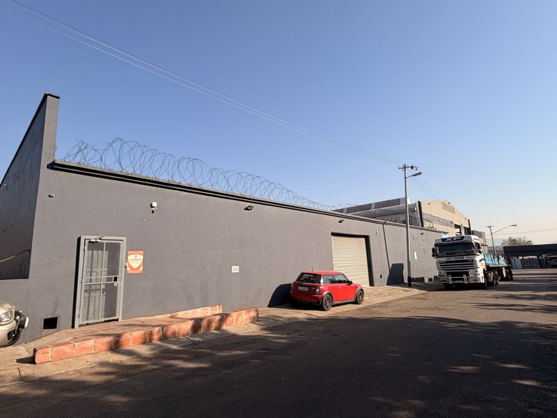 Commercial property exterior featuring a secure grey facade, roller shutter access, and perimeter razor wire fencing.