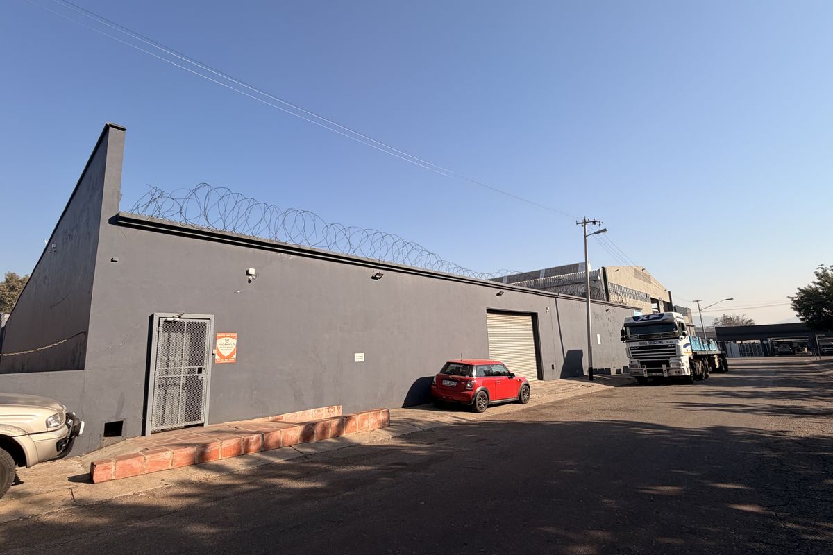 Commercial property exterior featuring a secure grey facade, roller shutter access, and perimeter razor wire fencing.