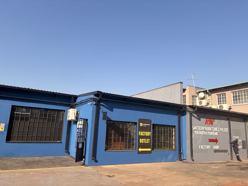 Commercial factory outlet building featuring blue painted masonry, industrial steel-framed windows, and paved driveway access.