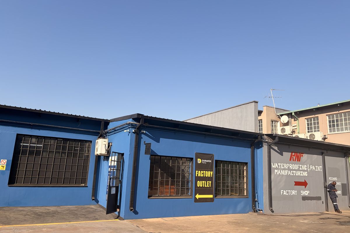Commercial factory outlet building featuring blue painted masonry, industrial steel-framed windows, and paved driveway access.