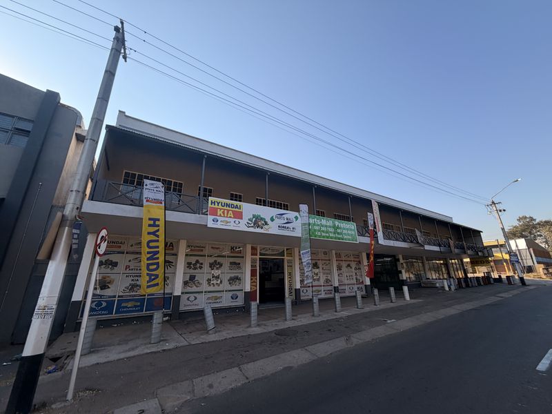 A commercial building facade featuring a ground-level storefront and an upper-level balcony with metal railings, situated along a street.