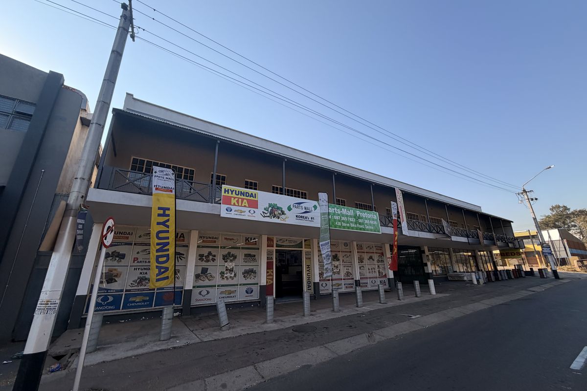 A commercial building facade featuring a ground-level storefront and an upper-level balcony with metal railings, situated along a street.