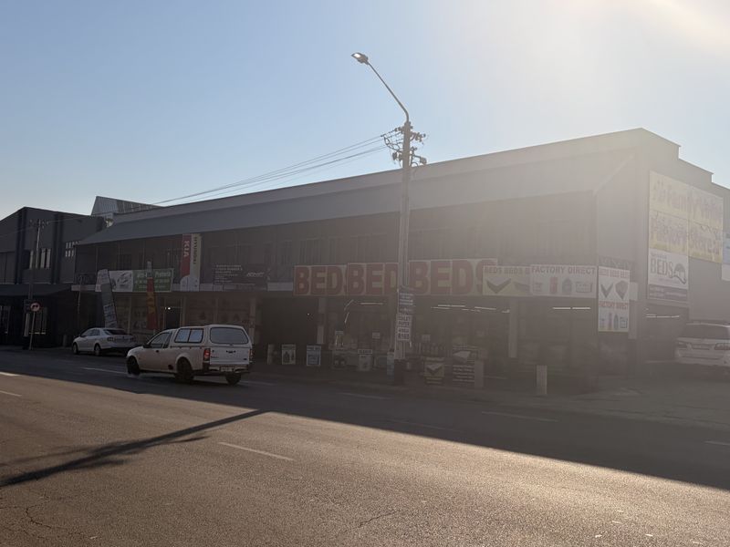 Street-level view of a commercial building featuring multiple storefronts with signage, situated along a paved road with sidewalk access.