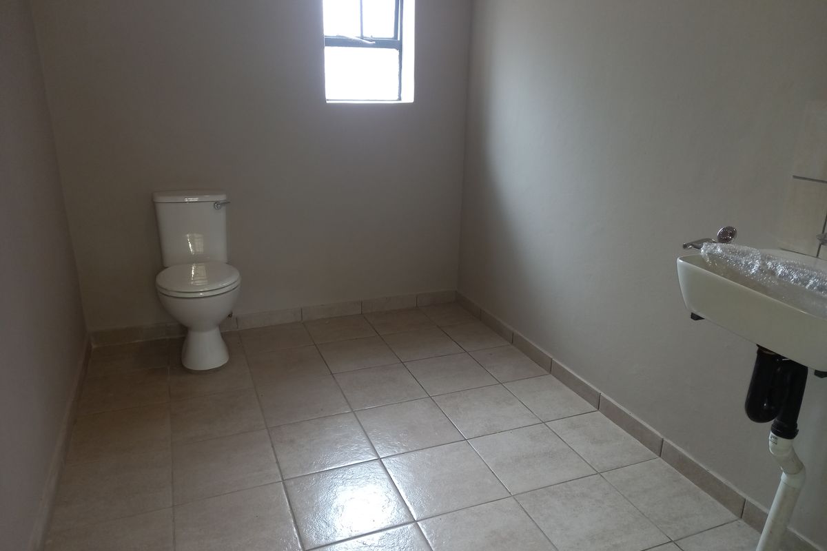 A simple, functional office bathroom featuring tiled flooring, a standard toilet, and a wall-mounted washbasin.