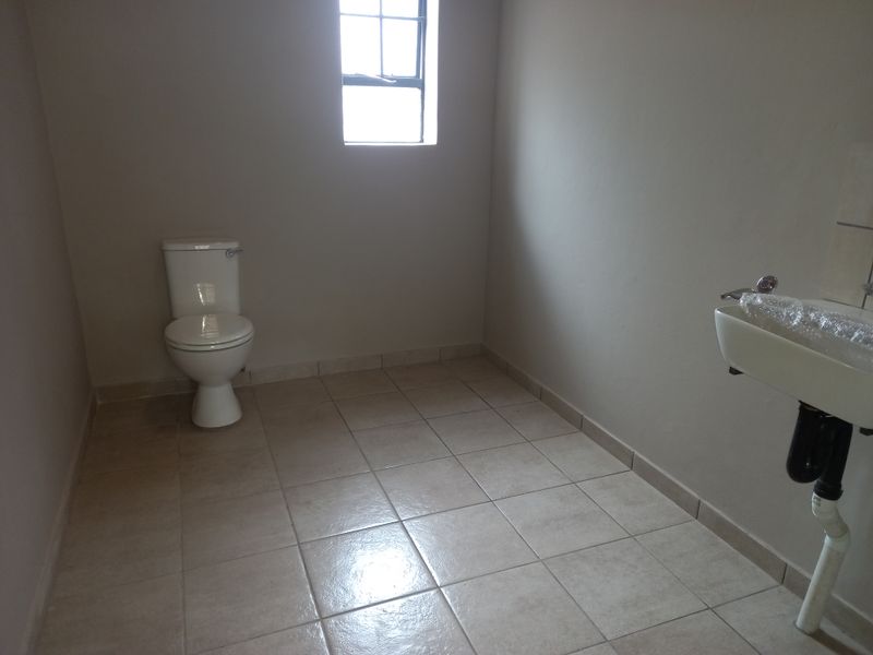 A simple, functional office bathroom featuring tiled flooring, a standard toilet, and a wall-mounted washbasin.