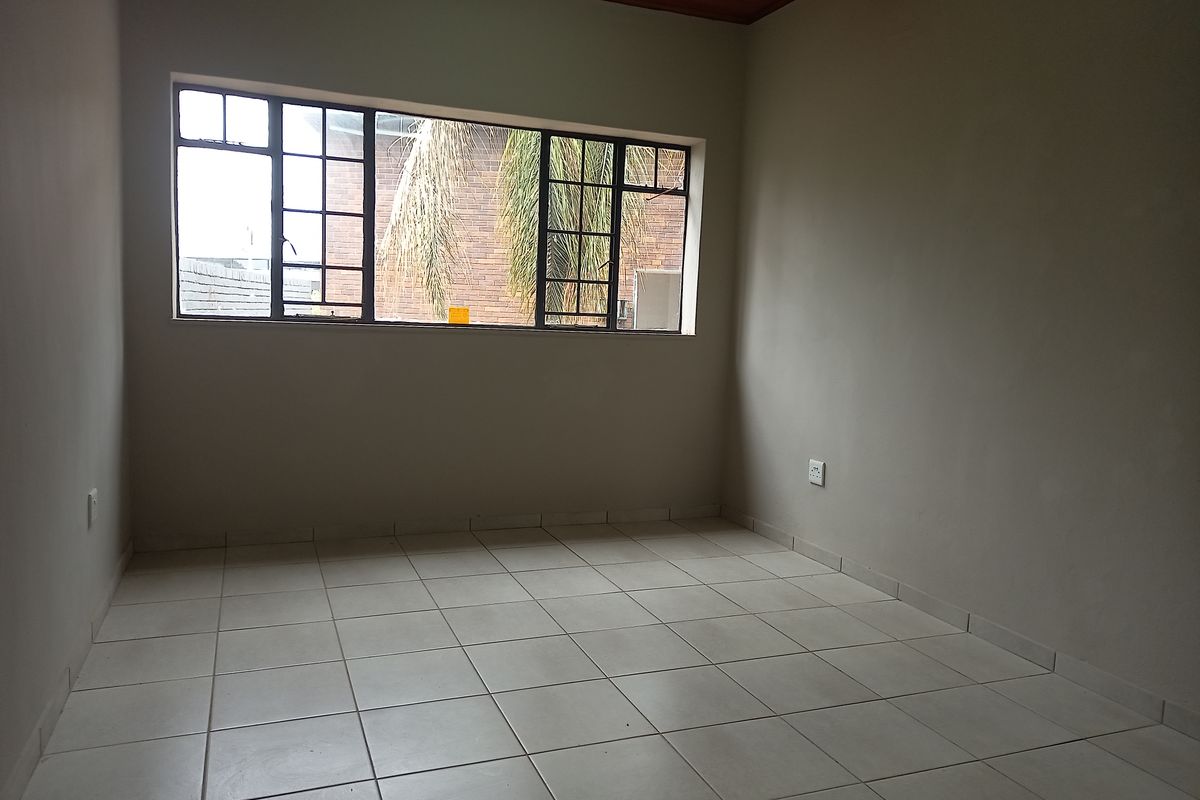 A clean, empty office space featuring neutral tiled flooring, a warm timber ceiling, and a large steel-framed window providing natural light.