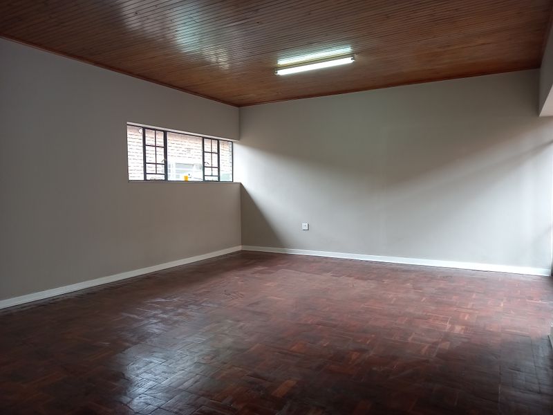 A spacious, empty office area featuring classic parquet flooring and a warm timber tongue and groove ceiling with a functional fluorescent light fixture.