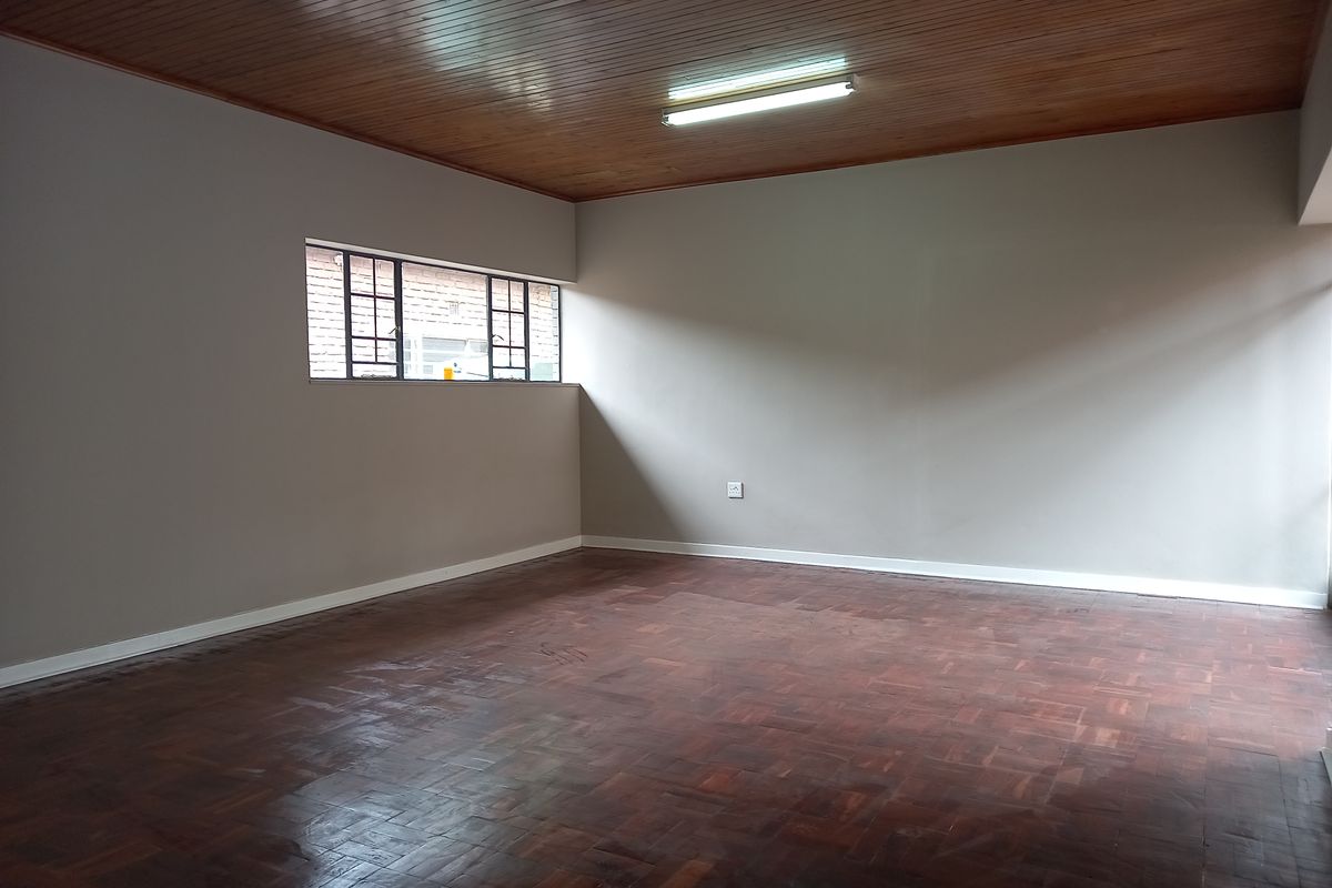 A spacious, empty office area featuring classic parquet flooring and a warm timber tongue and groove ceiling with a functional fluorescent light fixture.
