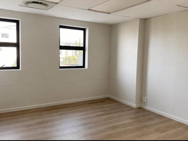 A bright, empty office space featuring modern laminate flooring, neutral walls, and a suspended ceiling with integrated air conditioning.