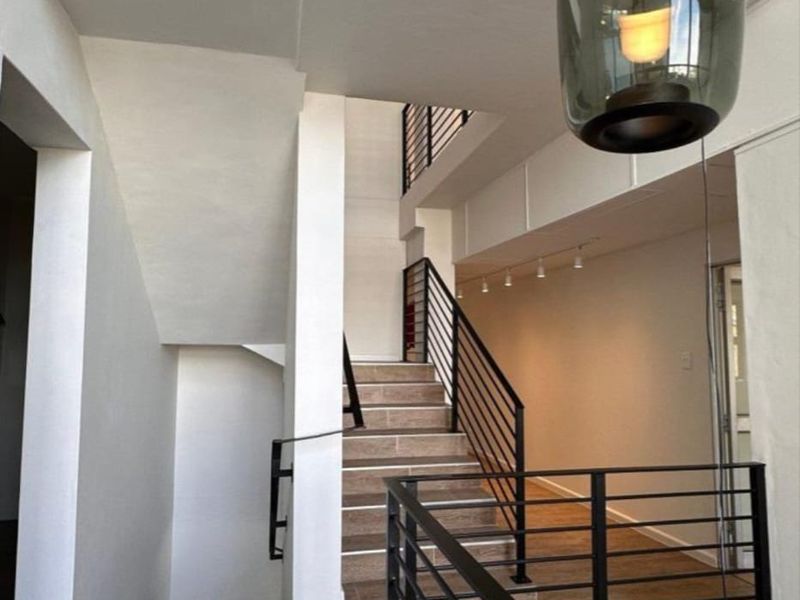 Modern office interior featuring a striking staircase with black metal balustrades, wood-look tile flooring, and contemporary pendant lighting in a bright, open-plan layout.