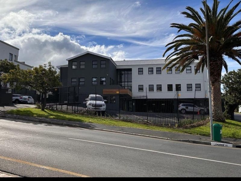 Front exterior view of a multi-story office building featuring a modern facade, secure perimeter fencing, and dedicated covered parking facilities.