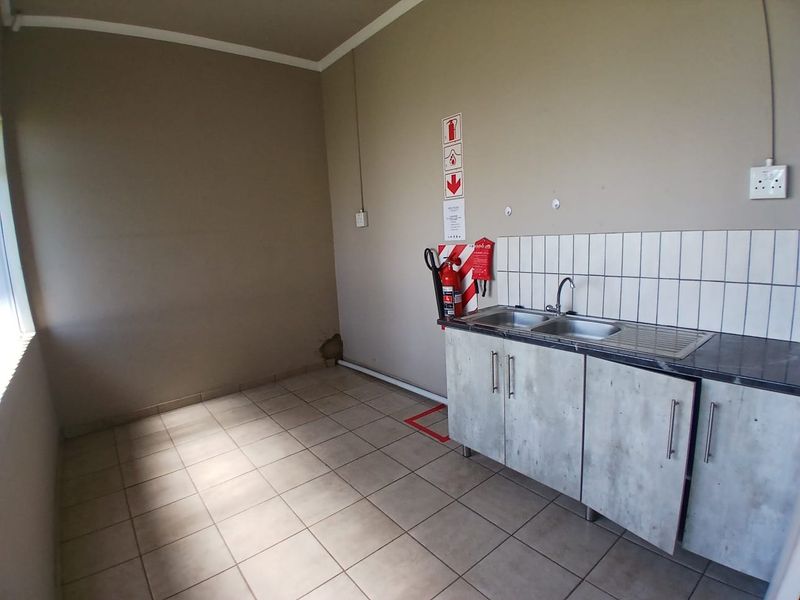 A functional office kitchenette featuring a stainless steel double sink, tiled splashback, and built-in cabinetry, with a fire safety station installed on the wall.