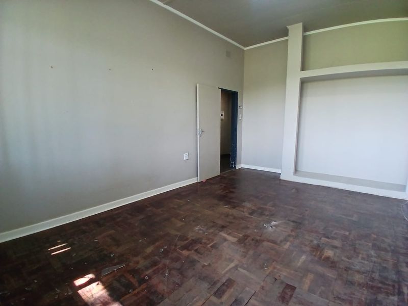 An empty office space featuring original parquet flooring and a built-in shelving unit, ready for refurbishment or custom fit-out.