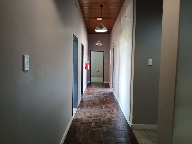 A functional office hallway featuring warm timber ceiling paneling, classic parquet flooring, and built-in storage cupboards, providing access to multiple office rooms.