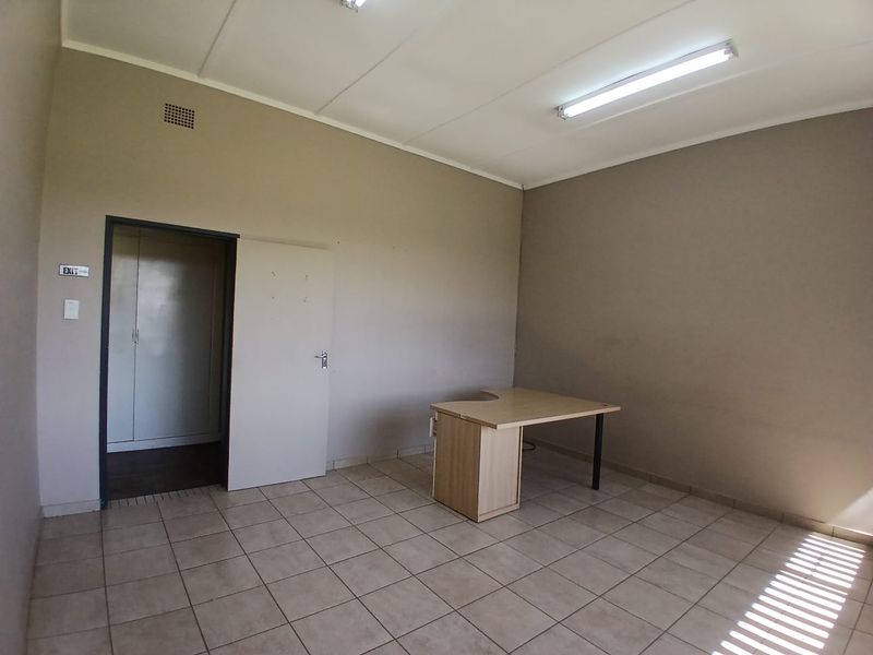 A functional office space featuring neutral wall tones, durable tiled flooring, and overhead fluorescent lighting, providing a clean and professional work environment.