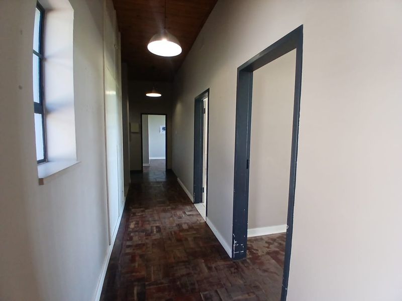 A spacious hallway featuring classic parquet flooring, a warm timber ceiling, and built-in storage cupboards, providing access to multiple office rooms.