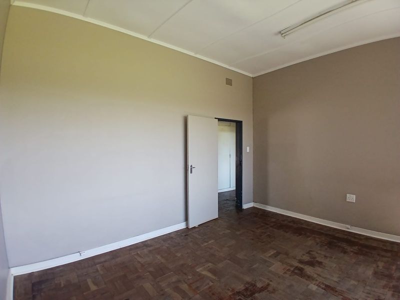 An empty office space featuring parquet flooring, neutral wall tones, and a functional overhead light fixture, ready for professional fit-out.