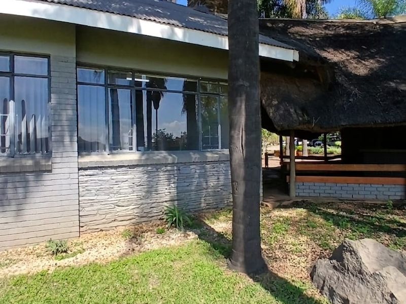 Rear view of the office building featuring a combination of thatched and metal roofing, stone cladding, and large windows overlooking the garden.