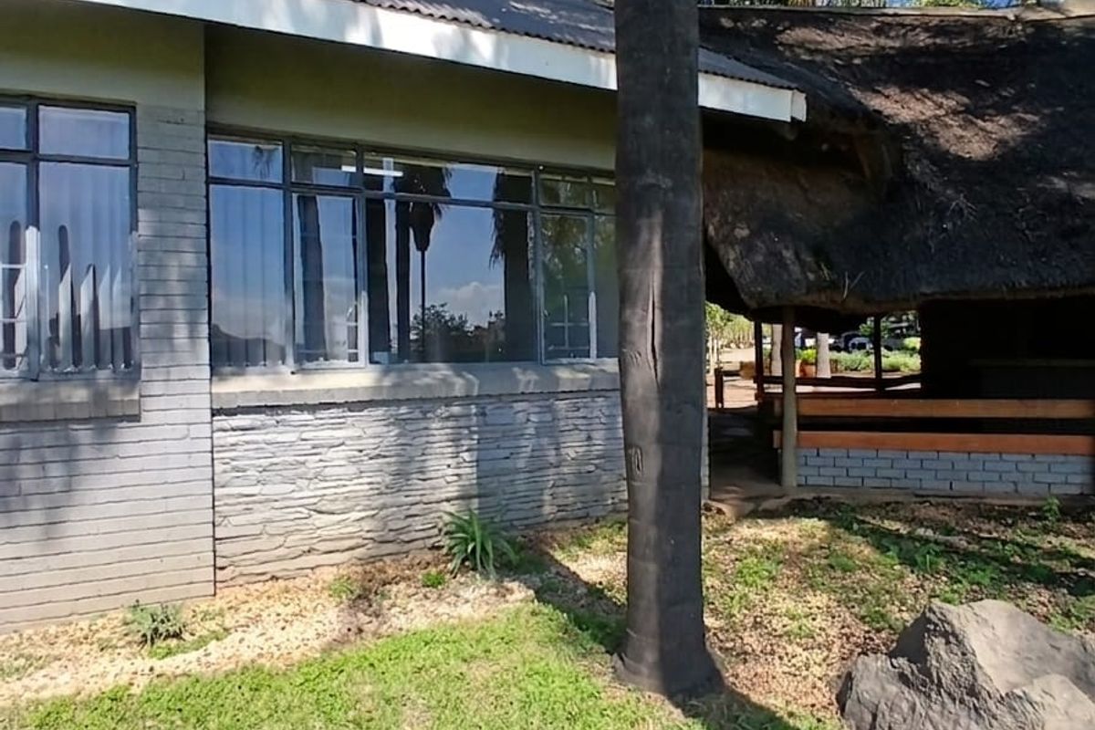 Rear view of the office building featuring a combination of thatched and metal roofing, stone cladding, and large windows overlooking the garden.