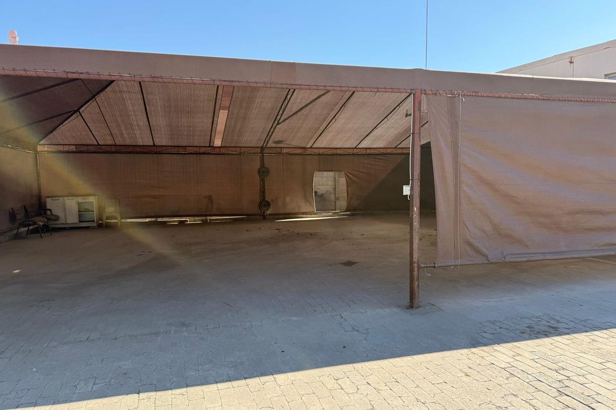 A large outdoor covered area featuring a metal frame structure with canvas shade covering and paved flooring, suitable for commercial storage or utility use.