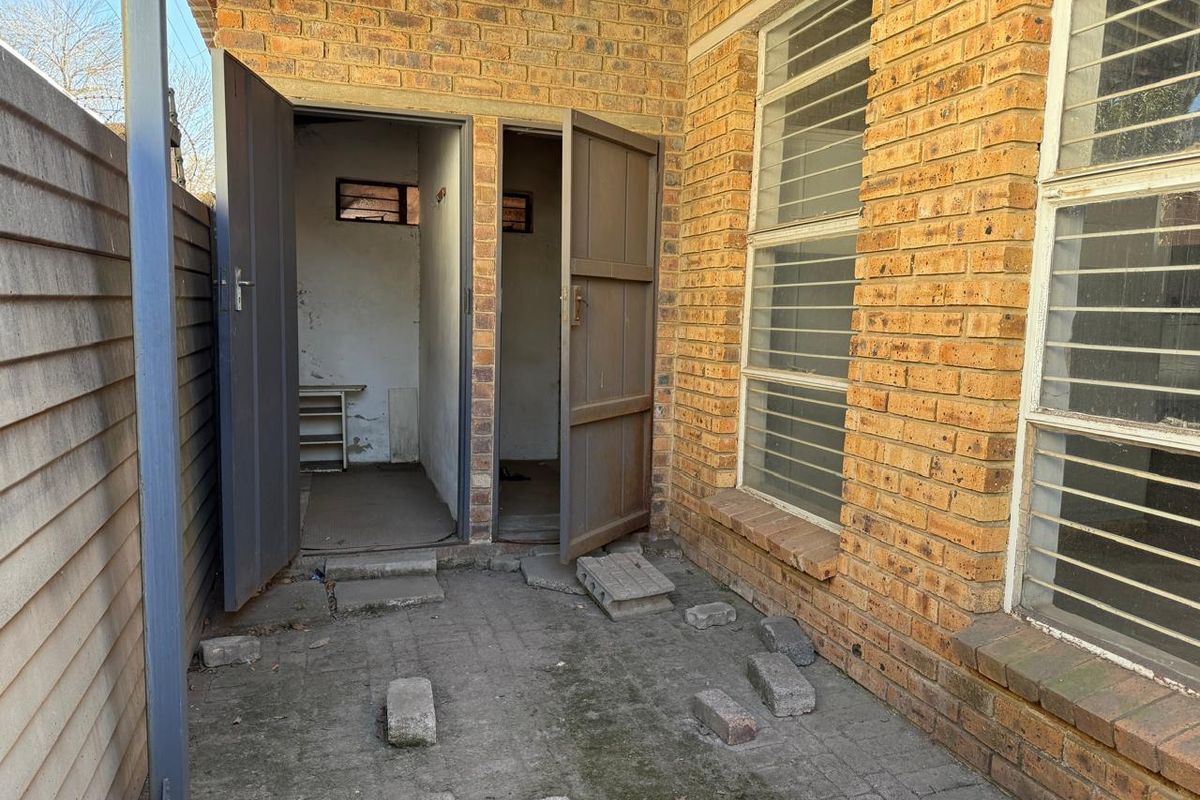 Rear exterior courtyard area featuring face brick walls, security-barred windows, and paved flooring with access to utility storage rooms.