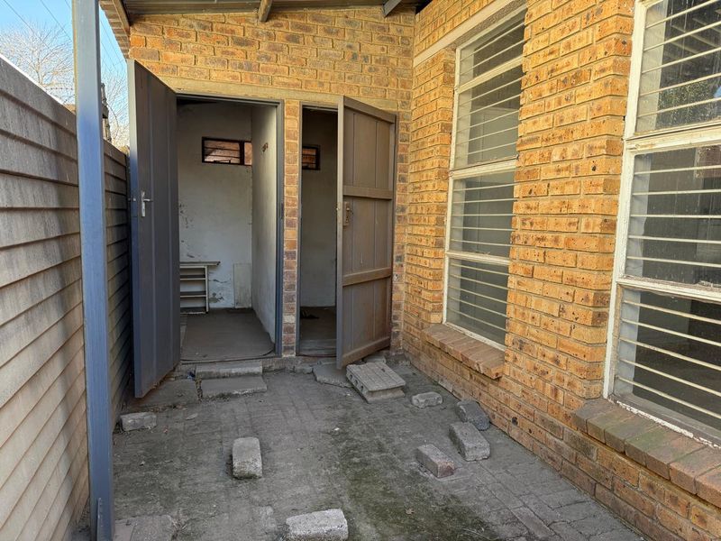Rear exterior courtyard area featuring face brick walls, security-barred windows, and paved flooring with access to utility storage rooms.