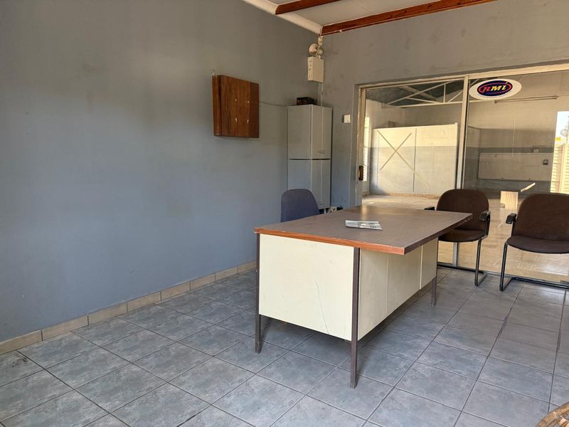 A functional commercial office space featuring tiled flooring and a sliding glass door leading to an adjacent workshop area.