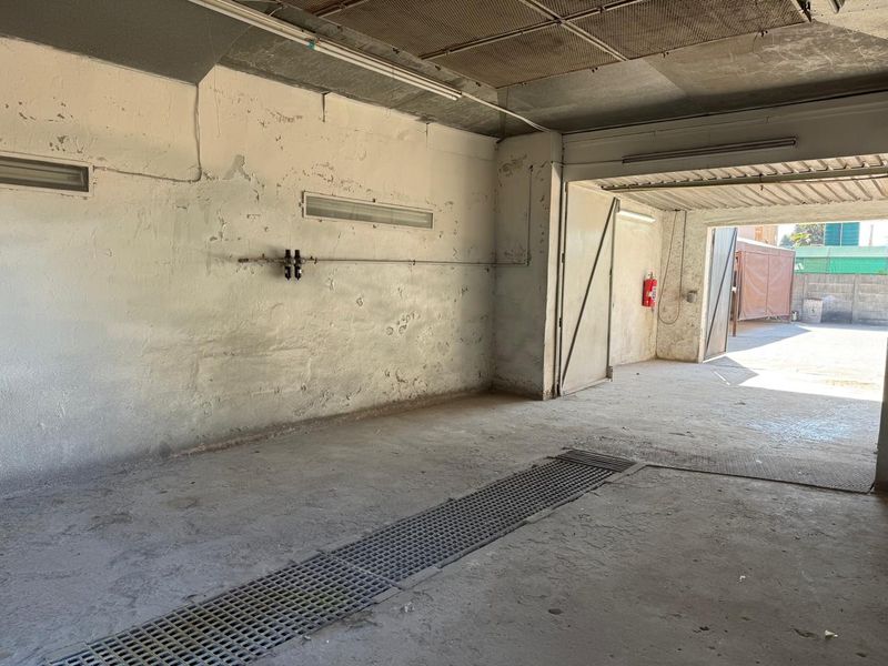 A spacious, industrial-style garage or utility workshop featuring a concrete floor with drainage, exposed ceiling, and wall-mounted fire safety equipment.