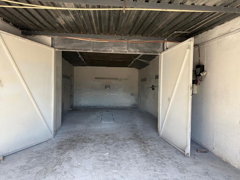 A spacious, empty commercial garage featuring large swing doors, a concrete floor with an inspection pit, and exposed ceiling infrastructure.