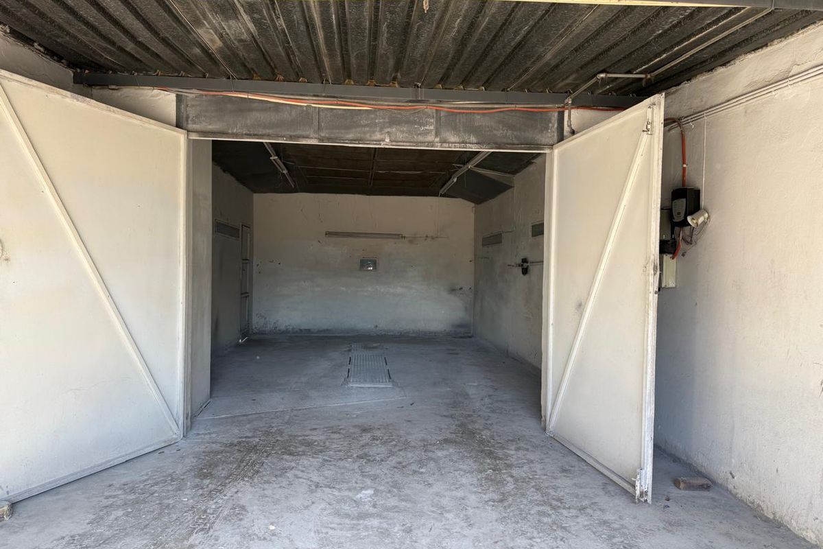 A spacious, empty commercial garage featuring large swing doors, a concrete floor with an inspection pit, and exposed ceiling infrastructure.