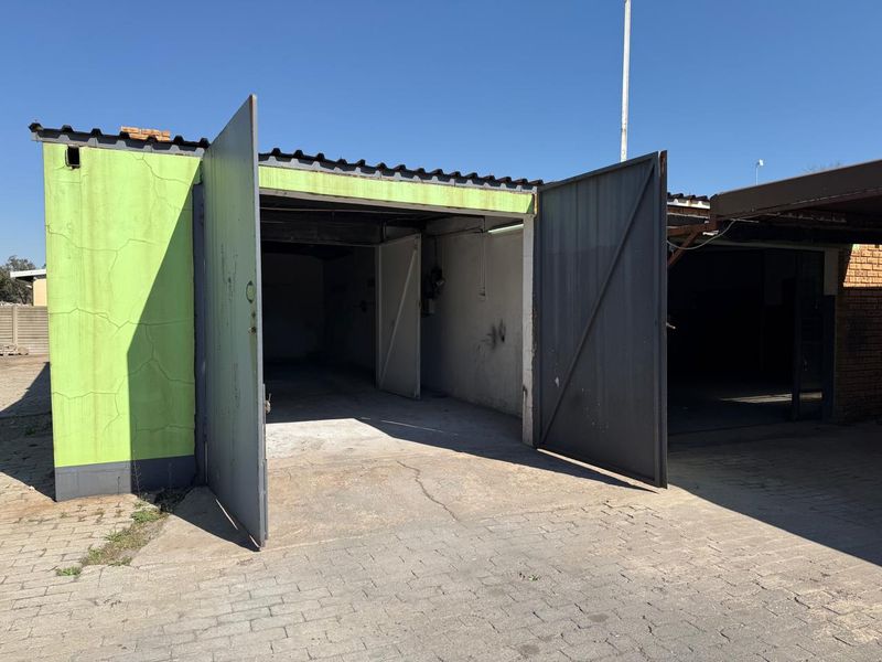 A commercial garage unit featuring metal swing doors, a corrugated roof, and a paved driveway, showing signs of wear and maintenance requirements.