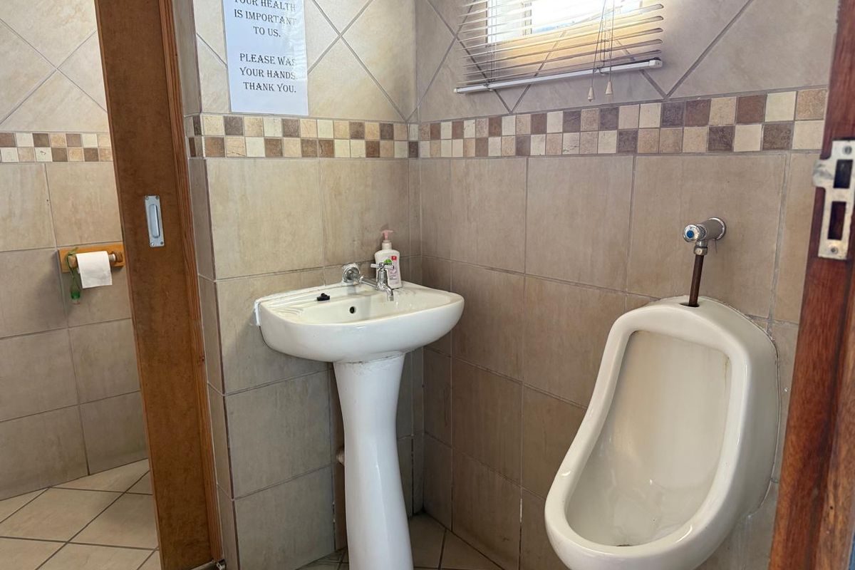 A functional commercial restroom featuring a pedestal washbasin, wall-mounted urinal, and neutral ceramic tiling throughout.