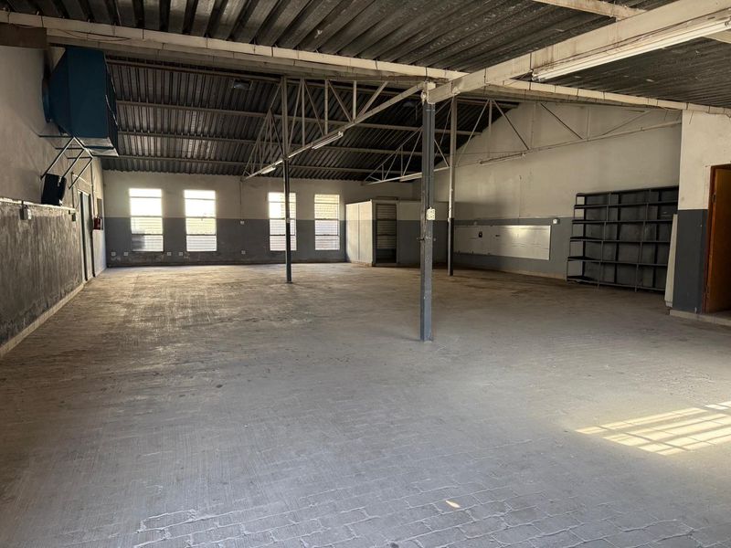 Spacious industrial utility space featuring exposed steel roof trusses, concrete flooring, and large windows, suitable for storage, workshop, or light commercial operations.