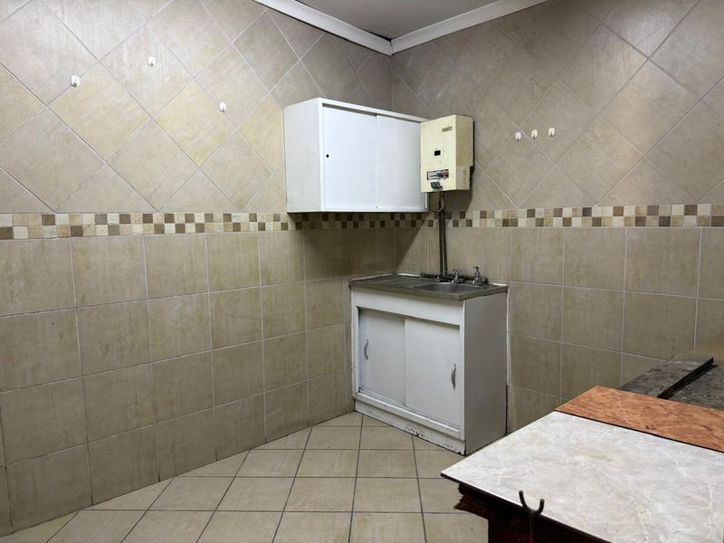 A functional laundry or utility area featuring tiled walls, a stainless steel sink, built-in cabinetry, and an electric water heater.