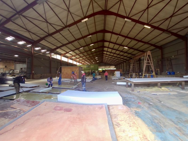 Large industrial warehouse space featuring a high-clearance steel portal frame structure, corrugated metal roofing, and expansive concrete flooring.