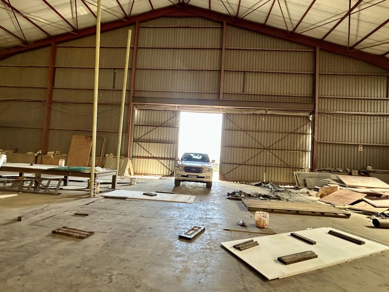 Spacious industrial warehouse featuring a steel portal frame, corrugated metal walls, concrete flooring, and a large sliding access door.