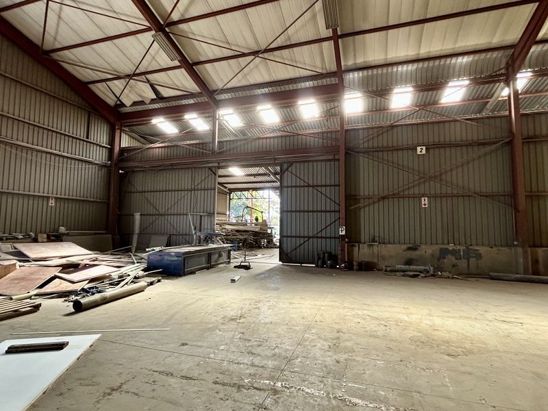 Spacious industrial warehouse unit featuring a high-clearance steel portal frame, concrete flooring, and large sliding access doors with natural light from overhead skylights.