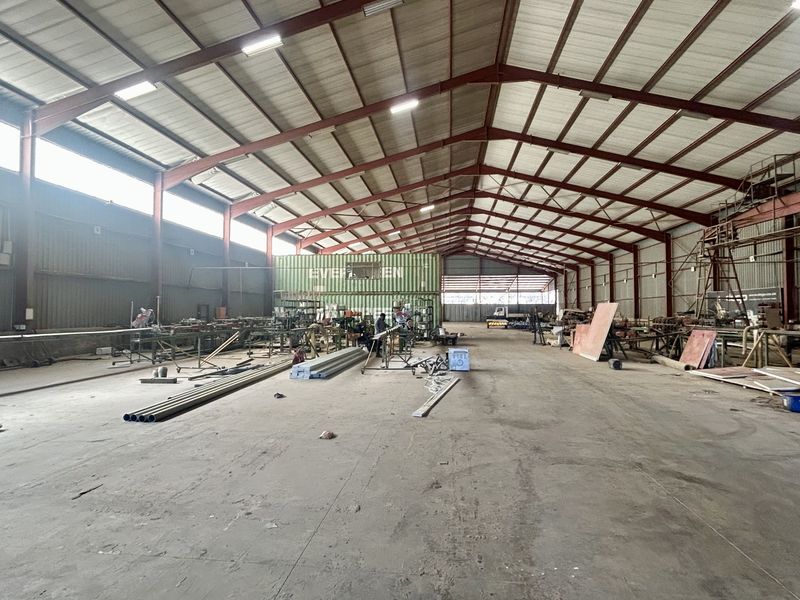 Spacious industrial warehouse featuring a steel portal frame, high ceilings with fluorescent lighting, concrete flooring, and an integrated shipping container office structure.