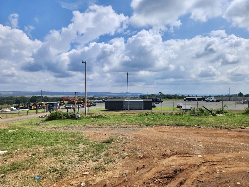 Wide view of an industrial yard featuring a gravel surface, perimeter fencing, and a modular office structure under a clear sky.