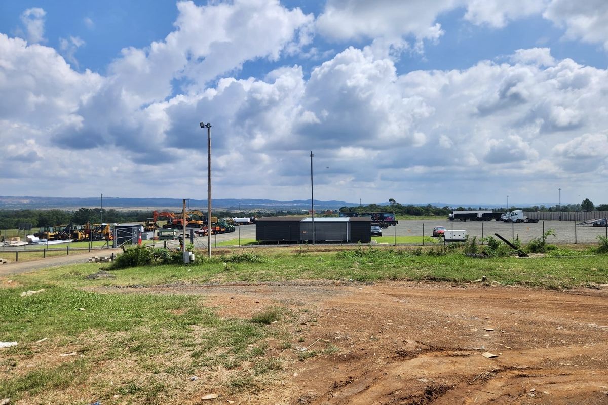 Wide view of an industrial yard featuring a gravel surface, perimeter fencing, and a modular office structure under a clear sky.