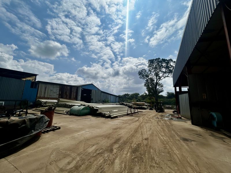 Industrial yard area featuring corrugated metal warehouse structures and concrete surfacing, suitable for storage or logistics operations.