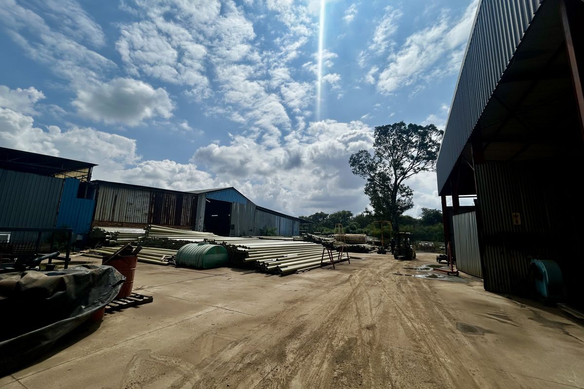 Industrial yard area featuring corrugated metal warehouse structures and concrete surfacing, suitable for storage or logistics operations.